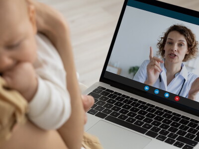 A mother holding her baby speaks with a physician via telehealth call.