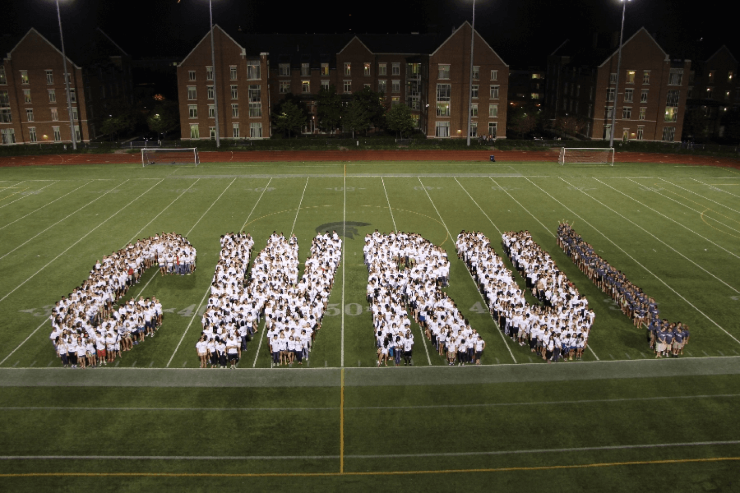 Students on football field spelling out CWRU in white with exclamation point in blue
