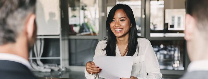 A young woman is smiling and holding a resume during a corporate job interview.