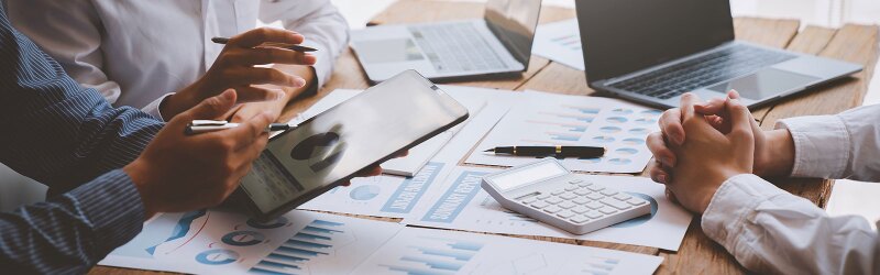A financial analyst analyzes a business financial report on a digital tablet during a discussion.
