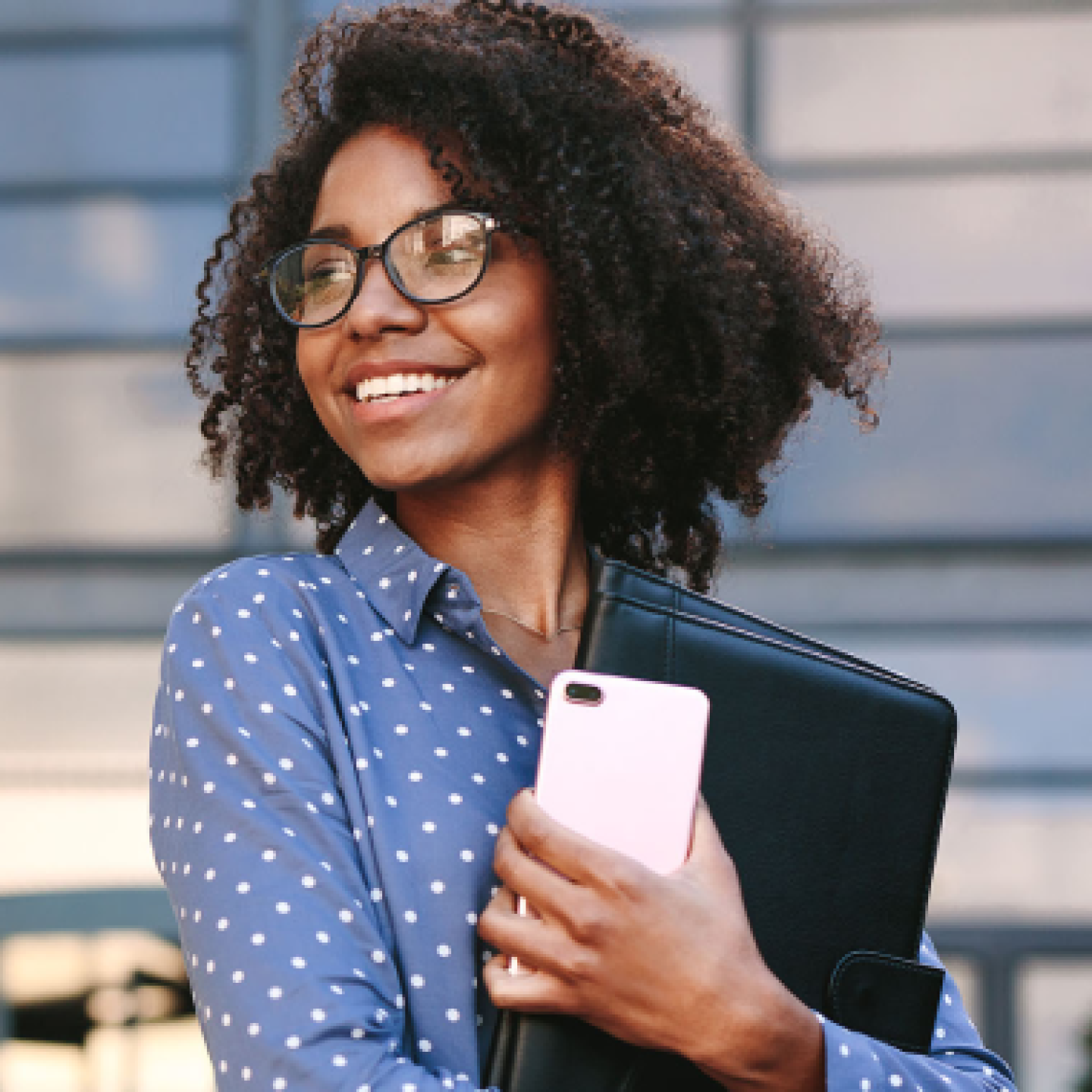 A close-up of a female entrepreneur smiling while holding a smartphone and binder in her arms.