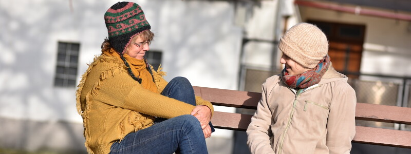 A social worker and her client talk while sitting outdoors in the fall.