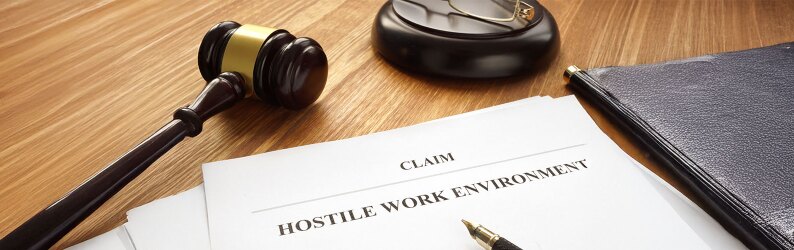 A document reading "Claim: Hostile Work Environment" is lying on a desk next to a gavel.