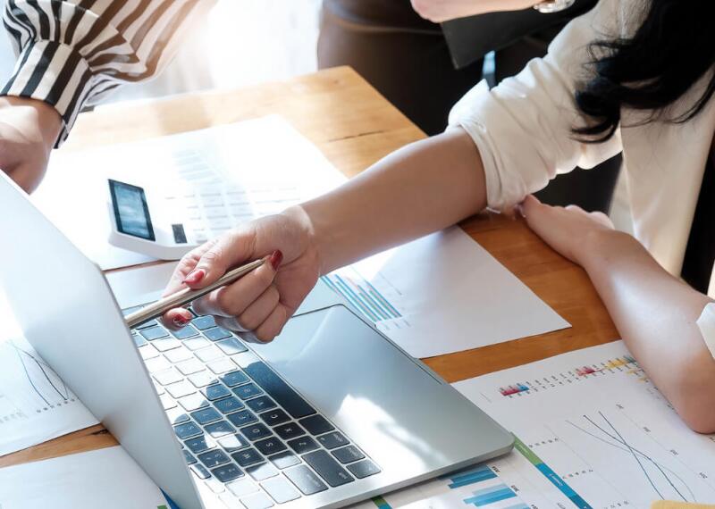Hand pointing at laptop screen with pen over graphs