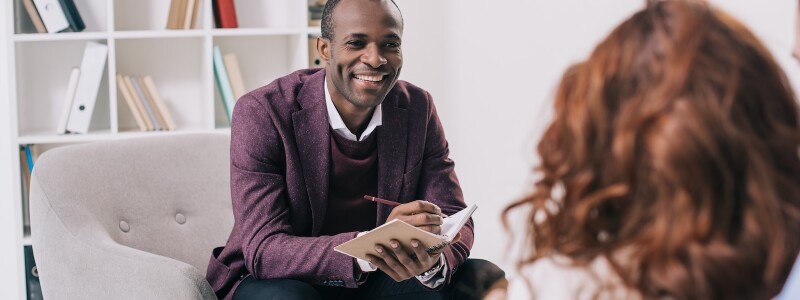 Smiling counselor takes notes while in session with a client