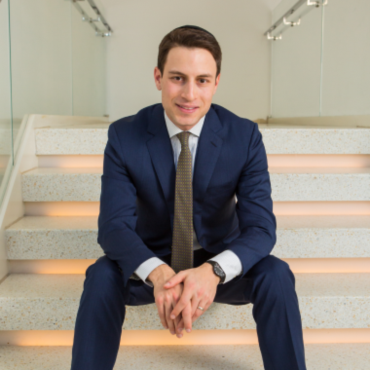 A male Yeshiva University real estate student is sitting on the stairs.
