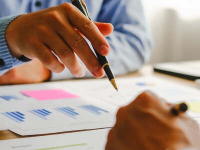 The hands of two tax professionals holding pens and pointing at graphs