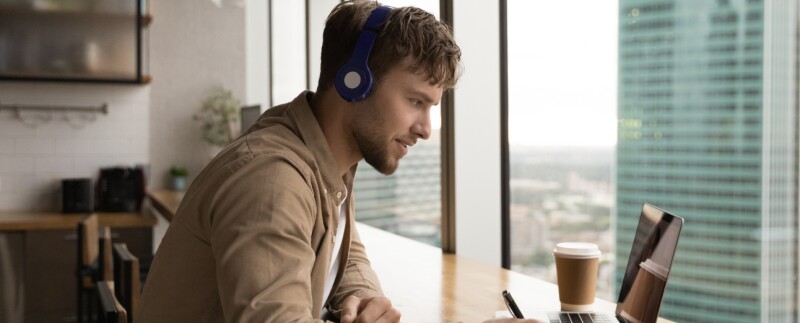 Man wearing headphones using laptop, studying online
