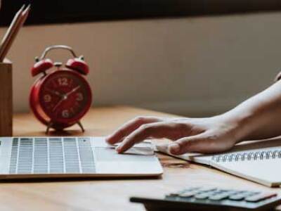 A seated student works on a laptop and a spiral notebook simultaneously