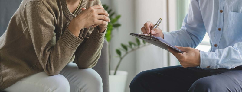 Close-up image of a man with a clipboard and pen sitting across from a woman.