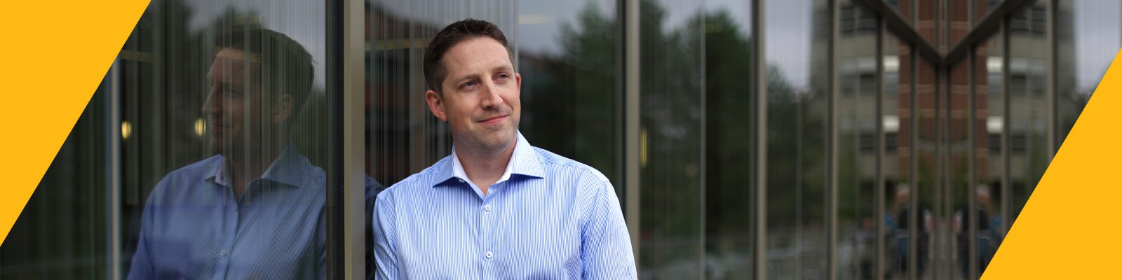 Professional smiles confidently while leaning against glass window of business building