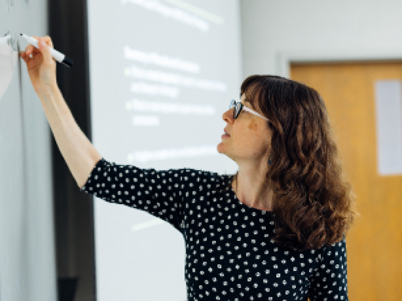 woman with glasses writing on a whiteboard