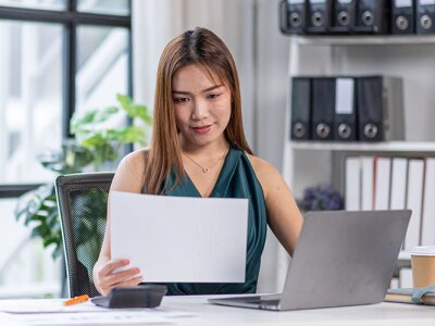 A woman sitting at a desk, reading a piece of paper.