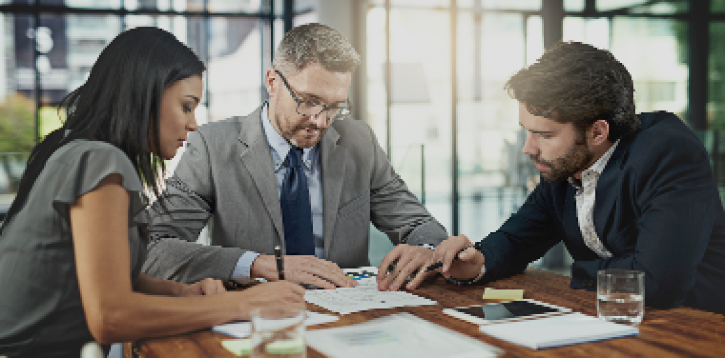 woman and 2 men meeting at a table with paperwork