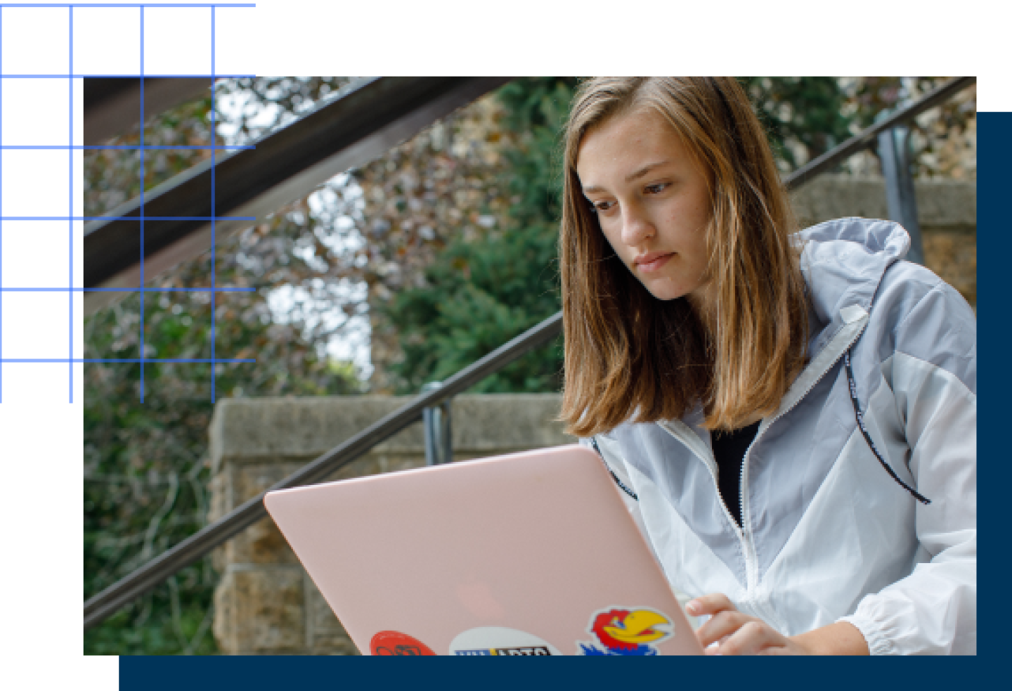 A female KU student sits on the campus steps looking at her laptop.