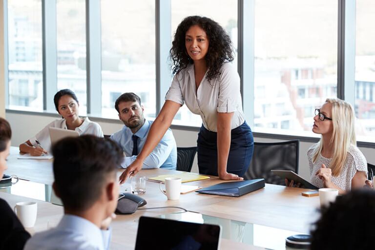 Woman standing at table leading discussion with seated colleagues