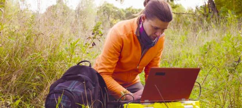 woman in an orange shirt on a laptop outdoors