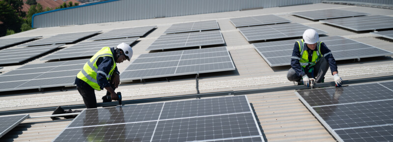 Two men in safety gear working on a field of solar panels