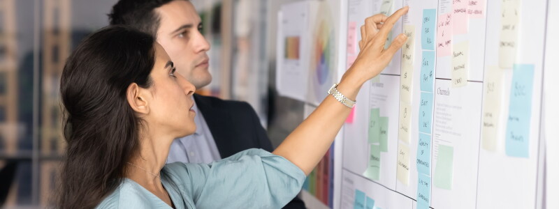 Project managers working on tasking at Kanban scrum board, discussing teamwork strategy
