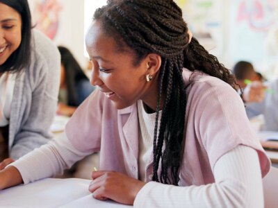 Happy teacher lends support to smiling female student in classroom