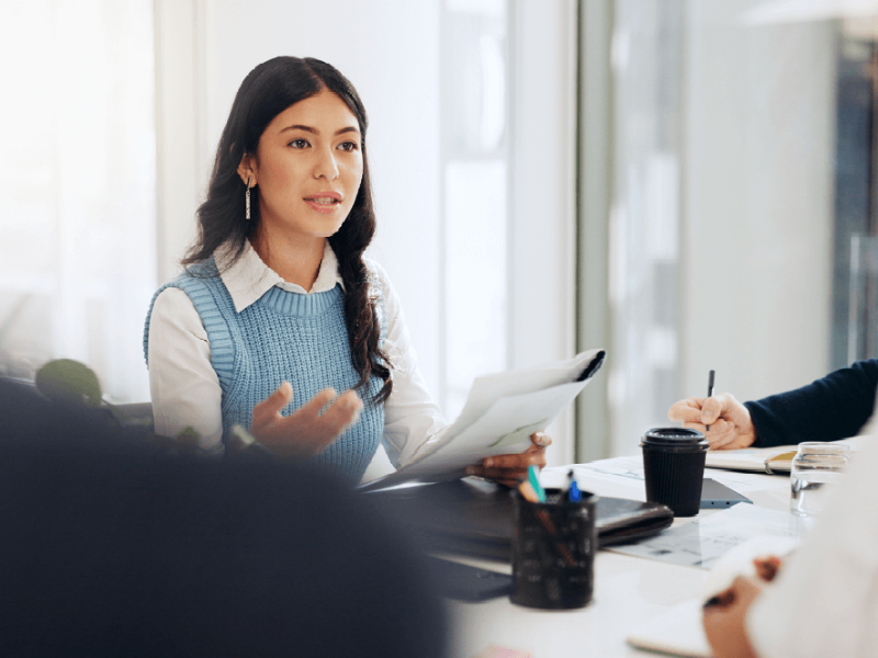 Woman in business attire leading a discussion at meeting table
