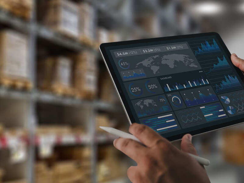 Logistics manager analyzing a supply chain data dashboard on a tablet inside a warehouse facility.