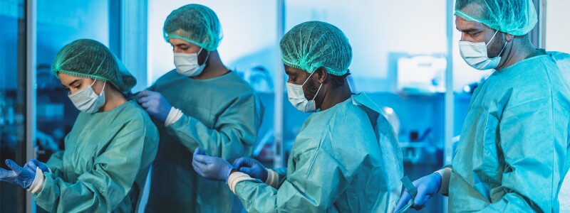 Four hospital staff members help each other put on their personal protective equipment.