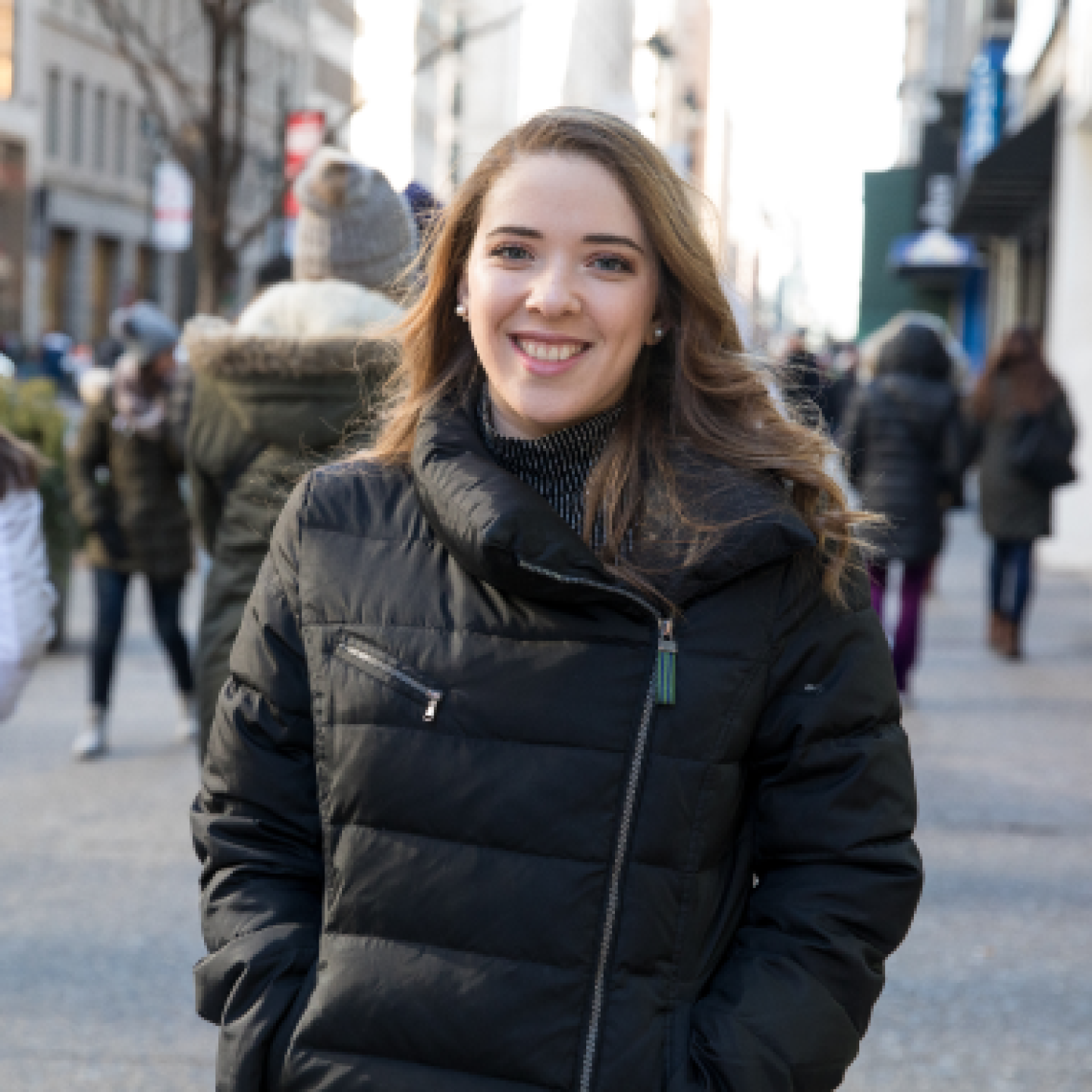 A female Yeshiva University is smiling while standing on a downtown sidewalk.