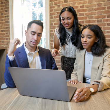 three people meeting at a table discussing information on a pc