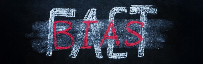 Erased word 'FACT' on a chalkboard, partially overwritten by the word 'BIAS' in red chalk