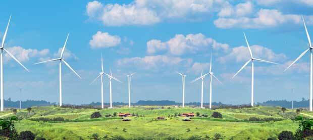 Windfarm windmills stand over meadows on a sunny, slightly cloudy day.