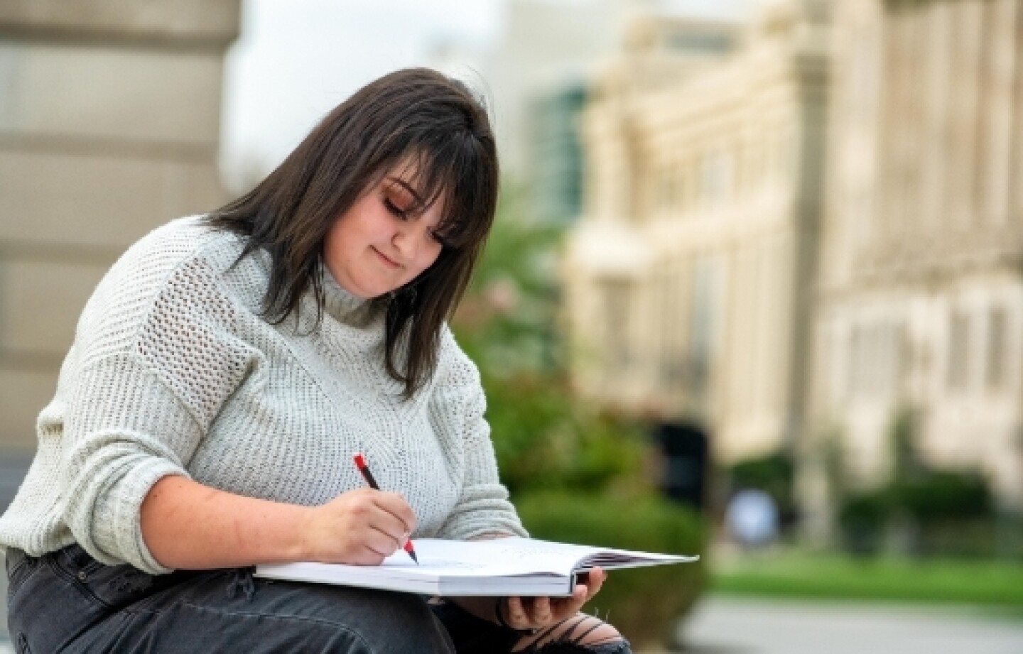 Woman wearing sweater sitting outside writing in book