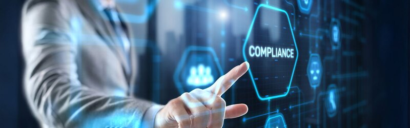 A hand in a suit points to a glowing hexagon with "compliance" on a futuristic blue digital interface.