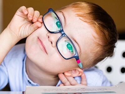 Young child with blue shirt and glasses tilting his head