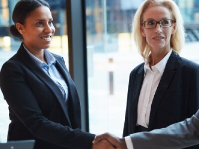 Two people shake hands in a group of diverse professionals