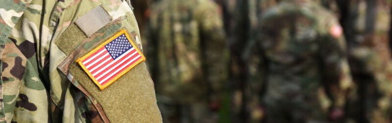 Close-up of an American soldier in uniform, standing in front of fellow soldiers.