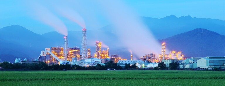 View of a factory in the middle of a green farmland in the early morning twilight ~ Factory pipes polluting air in a silent morning, a serious environmental issue