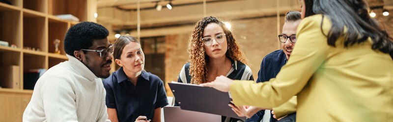 A diverse group of professionals engaged in a focused team meeting, reviewing a document together.