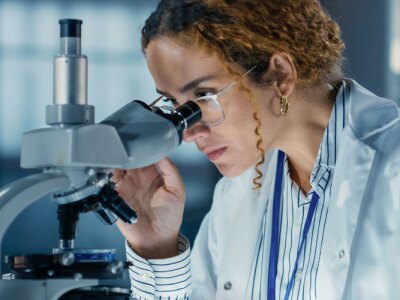 A female Biomedical Engineer in a lab testing Biological Samples under a microscope.