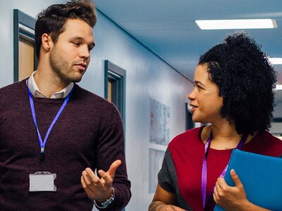 Two teachers are walking down a school hallway discussing teaching plans.