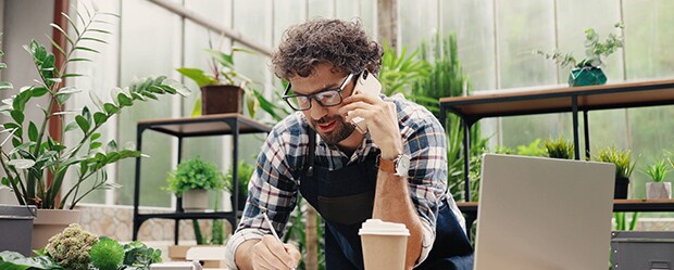 Happy caucasian male florist calling on smartphone at work.