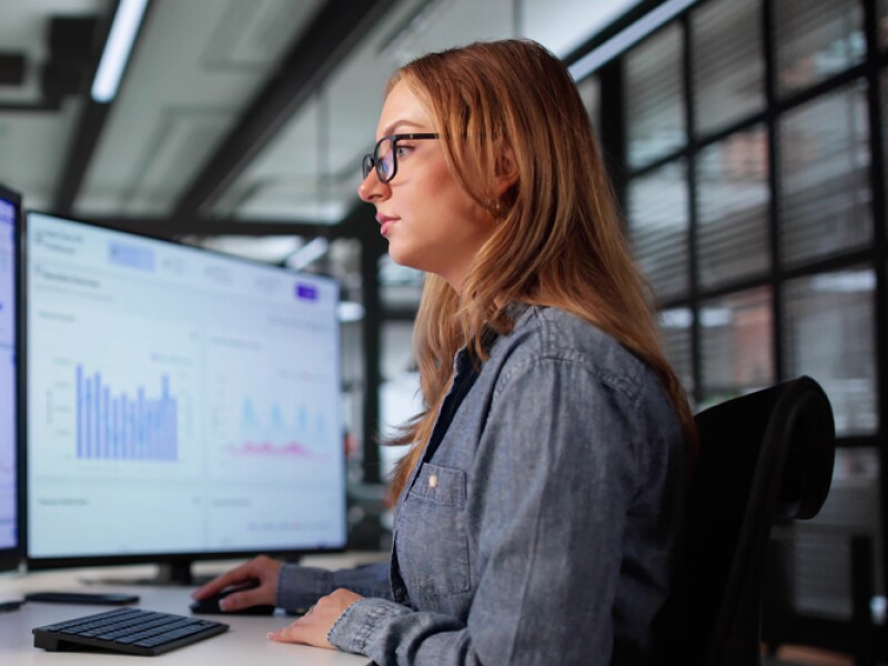 A young female data scientist analyzing financial data on computer screens.