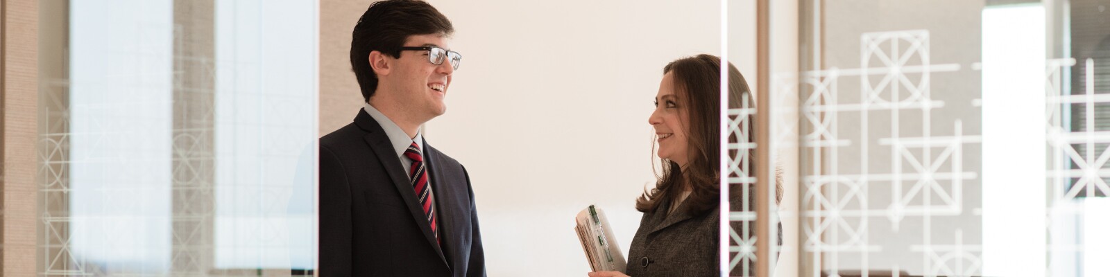 Two Marquette students speak to one another in business attire in a glass office space