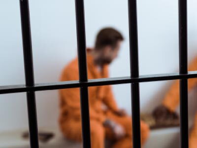 Two prisoners in orange jumpsuits sitting in a cell.