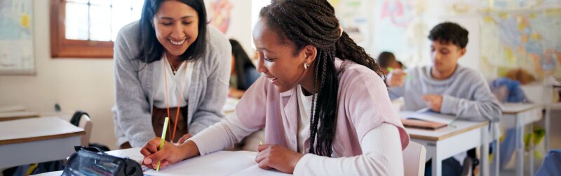 Happy teacher lends support to smiling female student in classroom