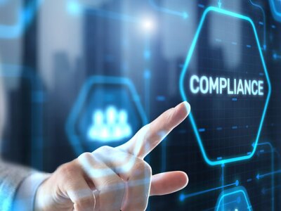 A hand in a suit points to a glowing hexagon with "compliance" on a futuristic blue digital interface.