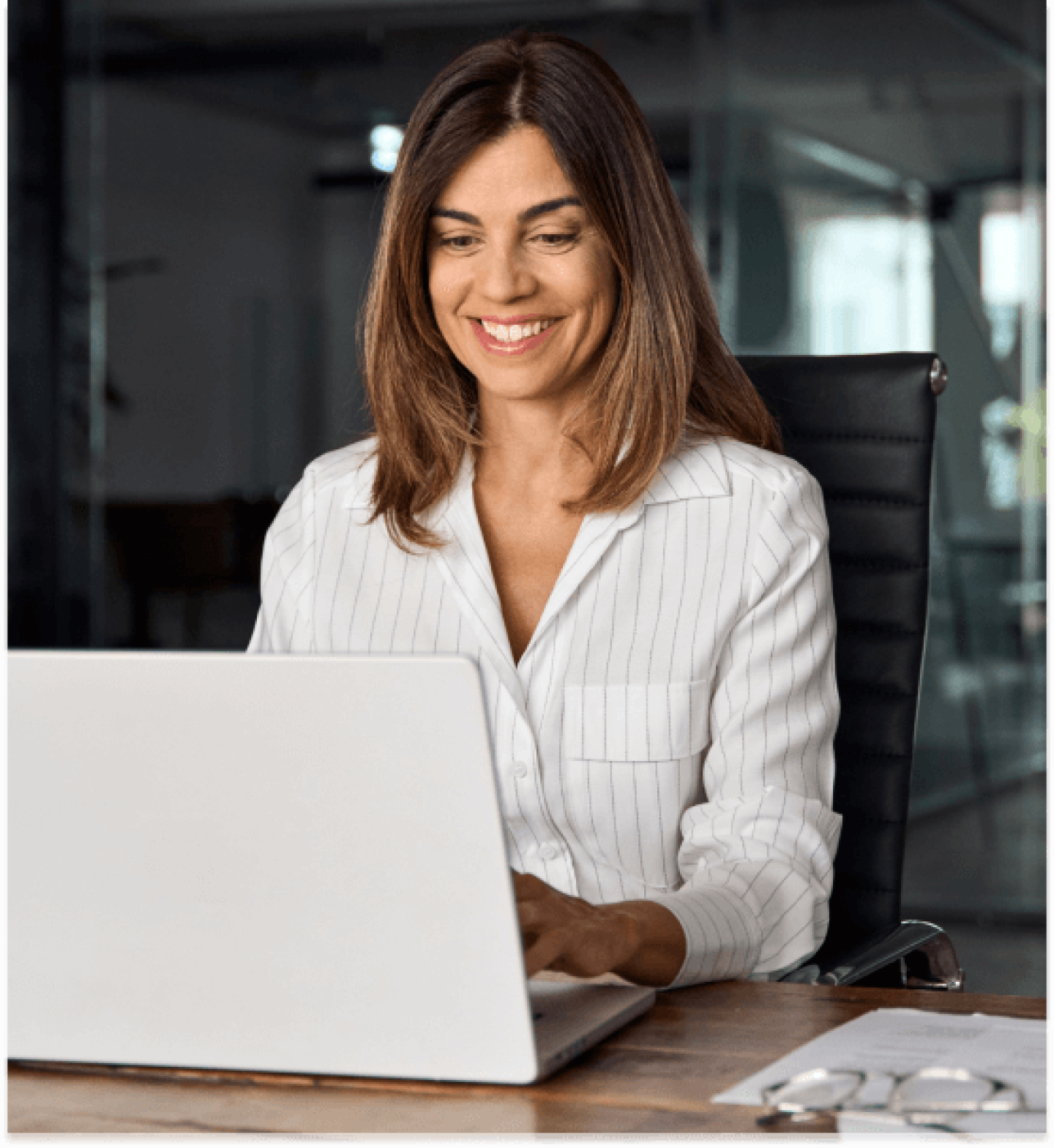 Woman in white shirt seated in office chair working on laptop