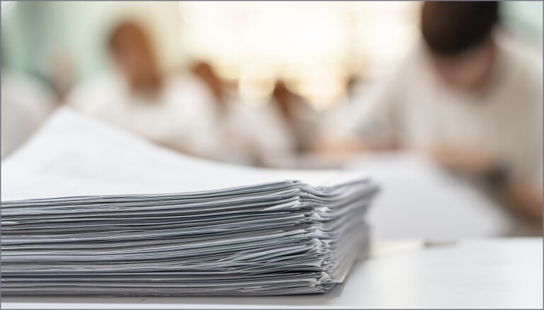 Stack of papers with students in background