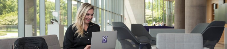 IMC graduate on laptop in the lobby of the Evanston campus