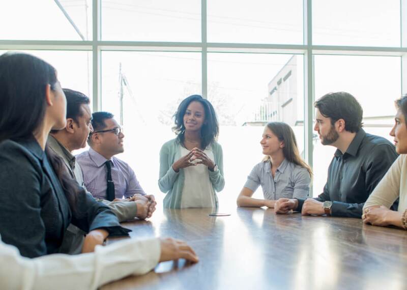 Woman speaking at head of table as colleagues listen